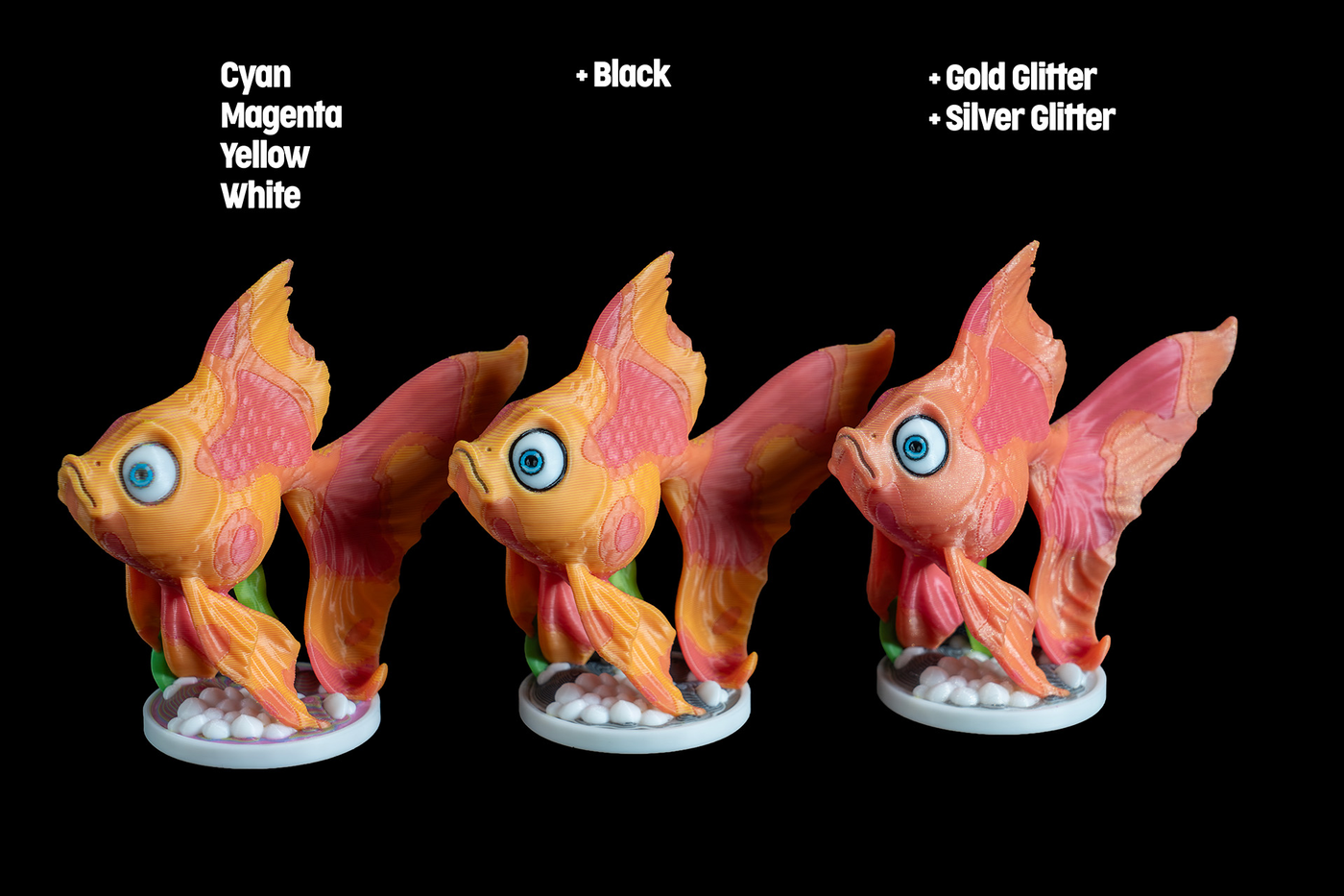 Three goldfish figurines with different colored eyes and fins, each on a white base with small white rocks.